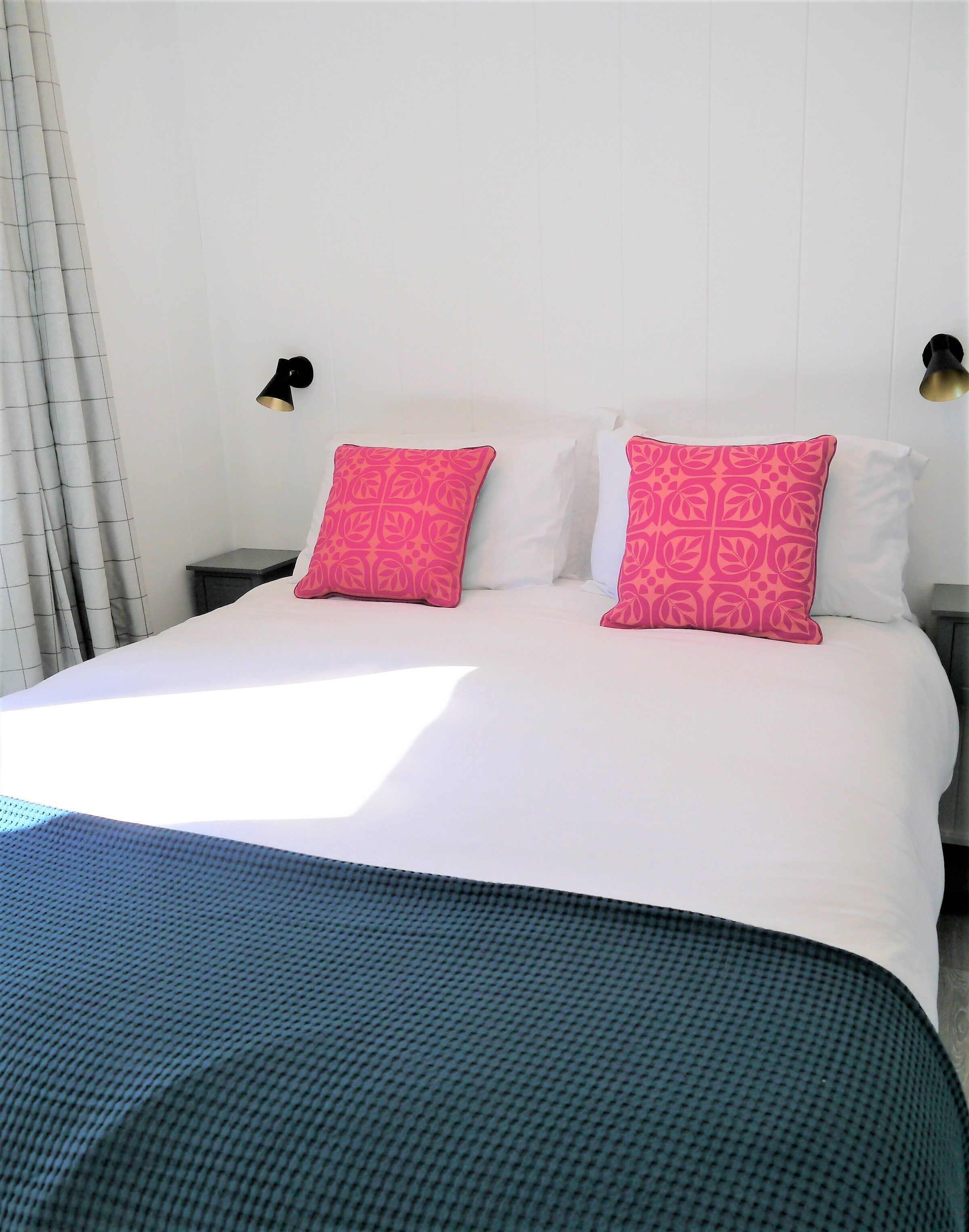 Un lit avec du linge de lit blanc et deux coussins à motifs roses, une couvre-lit bleu foncé et une table de chevet avec une lampe.