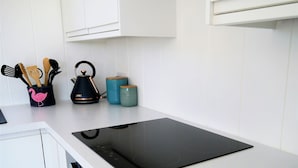 A kitchen with a black induction cooktop, a kettle, and a set of wooden utensils in a holder. - Sea Glass -  a lodge that sleeps 4 guests  in 2 bedrooms (Gatehouse of Fleet)