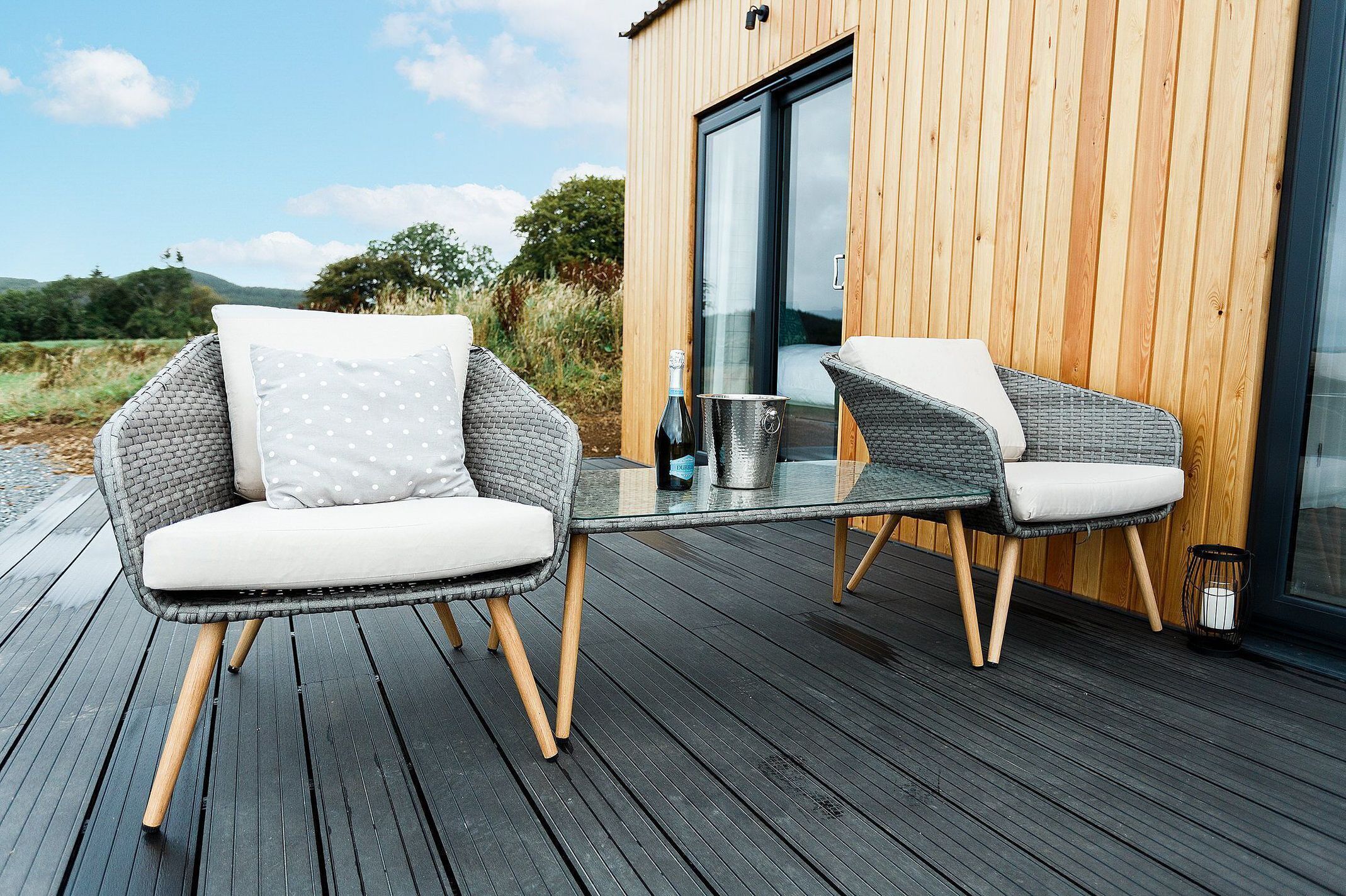 Une terrasse avec deux fauteuils en osier et une table, une bouteille de vin et un seau.