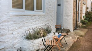 A white building with a window and a door, a small outdoor seating area with a table and chairs, and a sign that reads "THE MEW". - The Mew (Dartmouth)
