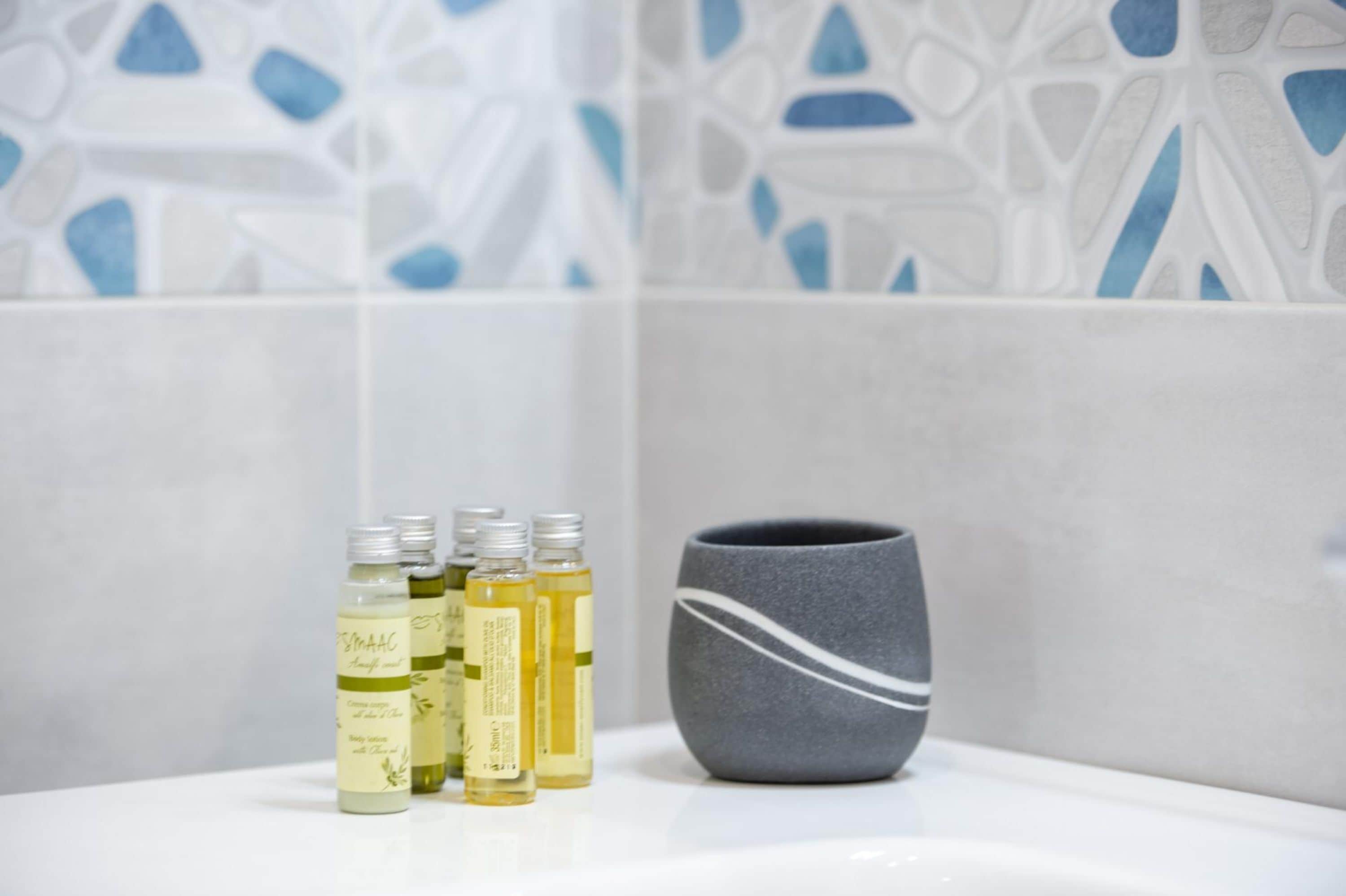 Une salle de bain avec un lavabo blanc, un récipient gris et quatre bouteilles de liquide, toutes munies d’étiquettes.