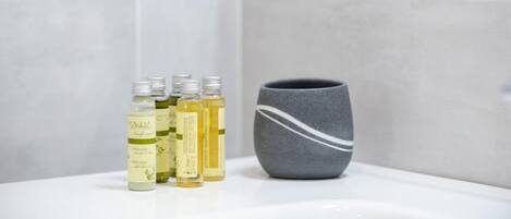 Une salle de bain avec un lavabo blanc, un récipient gris et quatre bouteilles de liquide, toutes munies d’étiquettes.