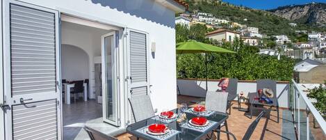 En balkon med et spisebord, en stol og en grøn parasol.