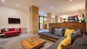 Un salon moderne avec un canapé rouge, un canapé gris et une table basse en bois. Un grand pilier se trouve au centre de la pièce, et un téléviseur est fixé au mur.