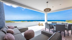 Un espace extérieur moderne et aménagé, avec vue sur l’océan, comprenant un ensemble de canapés, des fauteuils et une table.