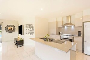 A modern kitchen with a central island, stainless steel appliances, and a decorative wall quote. - Family w/ Large Pool & Game Garage, Wlk to Beach (Cowes)