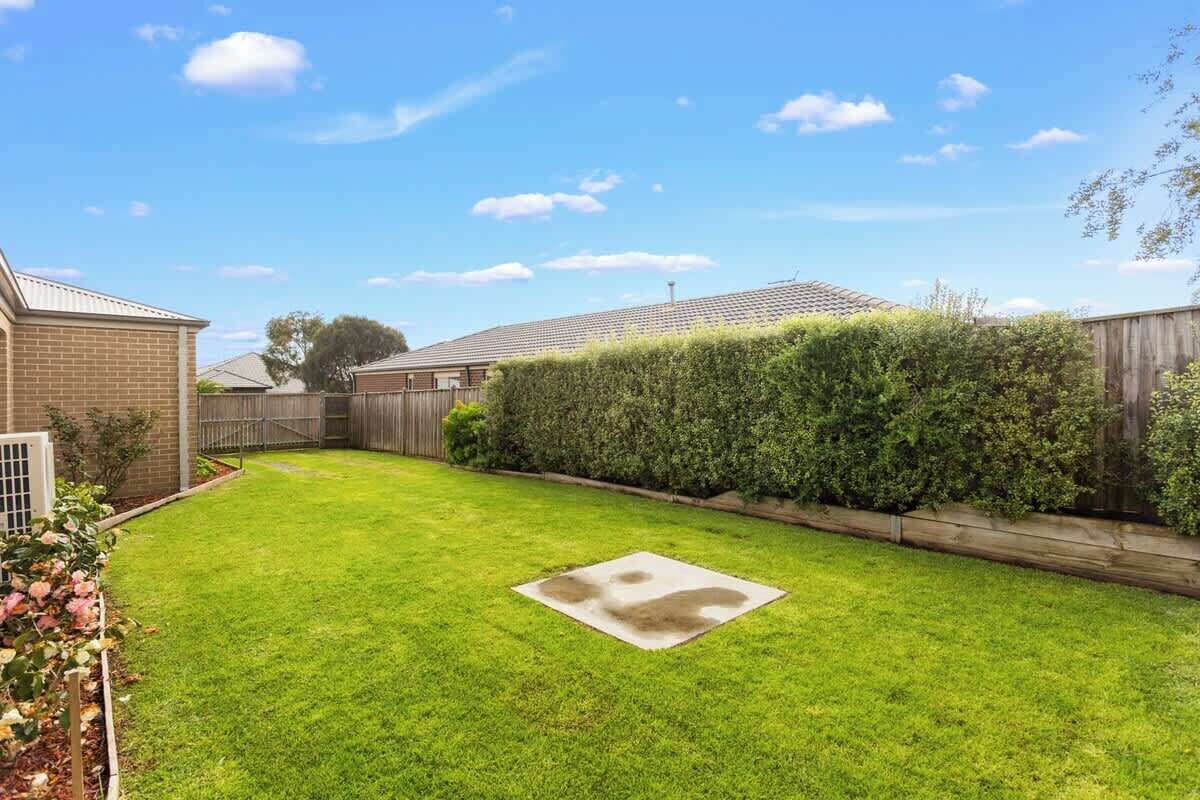 A backyard with a lawn, a wooden fence, and a brick building.