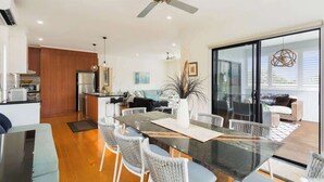 A modern kitchen with a built-in oven and a dining area with a glass table and wicker chairs. - Serene, Modern Beach Escape 3 Bed 2 Bath (Cape Woolamai)