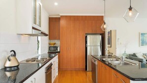 A modern kitchen with wooden cabinets, stainless steel appliances, and a black countertop. - Serene, Modern Beach Escape 3 Bed 2 Bath (Cape Woolamai)