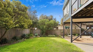 A backyard with a wooden deck, a grassy lawn, and a wooden fence. - Serene, Modern Beach Escape 3 Bed 2 Bath (Cape Woolamai)