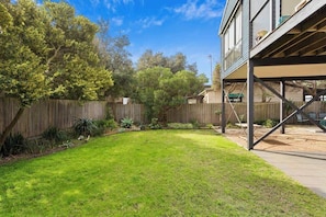 A backyard with a wooden deck, a grassy lawn, and a wooden fence. - Serene, Modern Beach Escape 3 Bed 2 Bath (Cape Woolamai)
