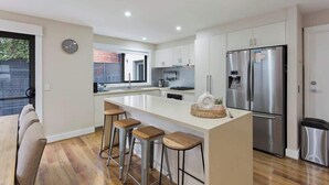 Une cuisine moderne dotée d’un îlot central, de tabourets de bar, d’appareils électroménagers en acier inoxydable et offrant une vue sur l’extérieur.