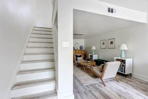 Una escalera conduce a una sala de estar con un sofá, sillas, una mesa de centro y una estantería.