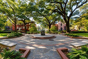 A courtyard with a central circular stone feature, surrounded by brick pathways and greenery.