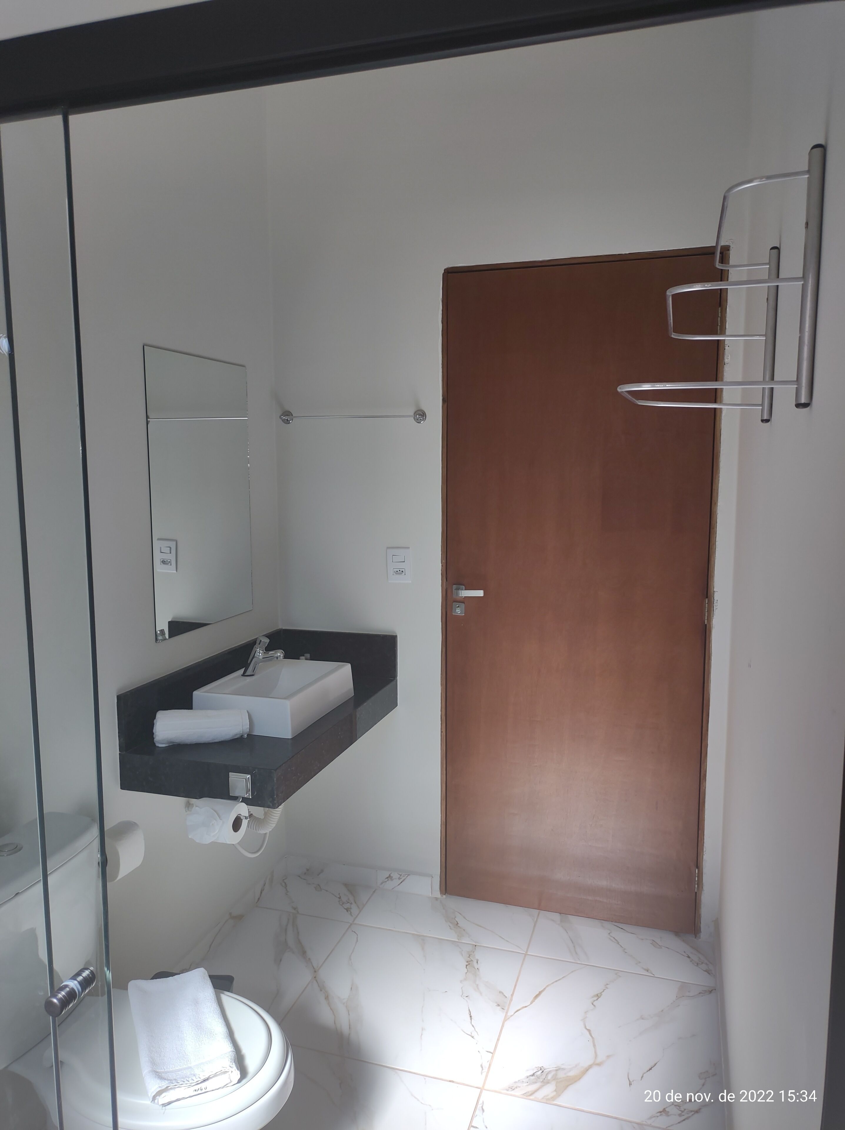 A modern bathroom with a glass shower enclosure, a white toilet, a vanity with a sink, and a wooden door.