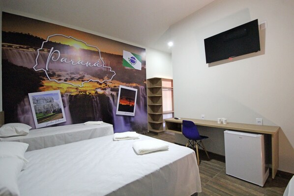 A hotel room with two beds, a desk, a chair, a TV, and a refrigerator. - Pousada das Bandeiras (Olímpia)