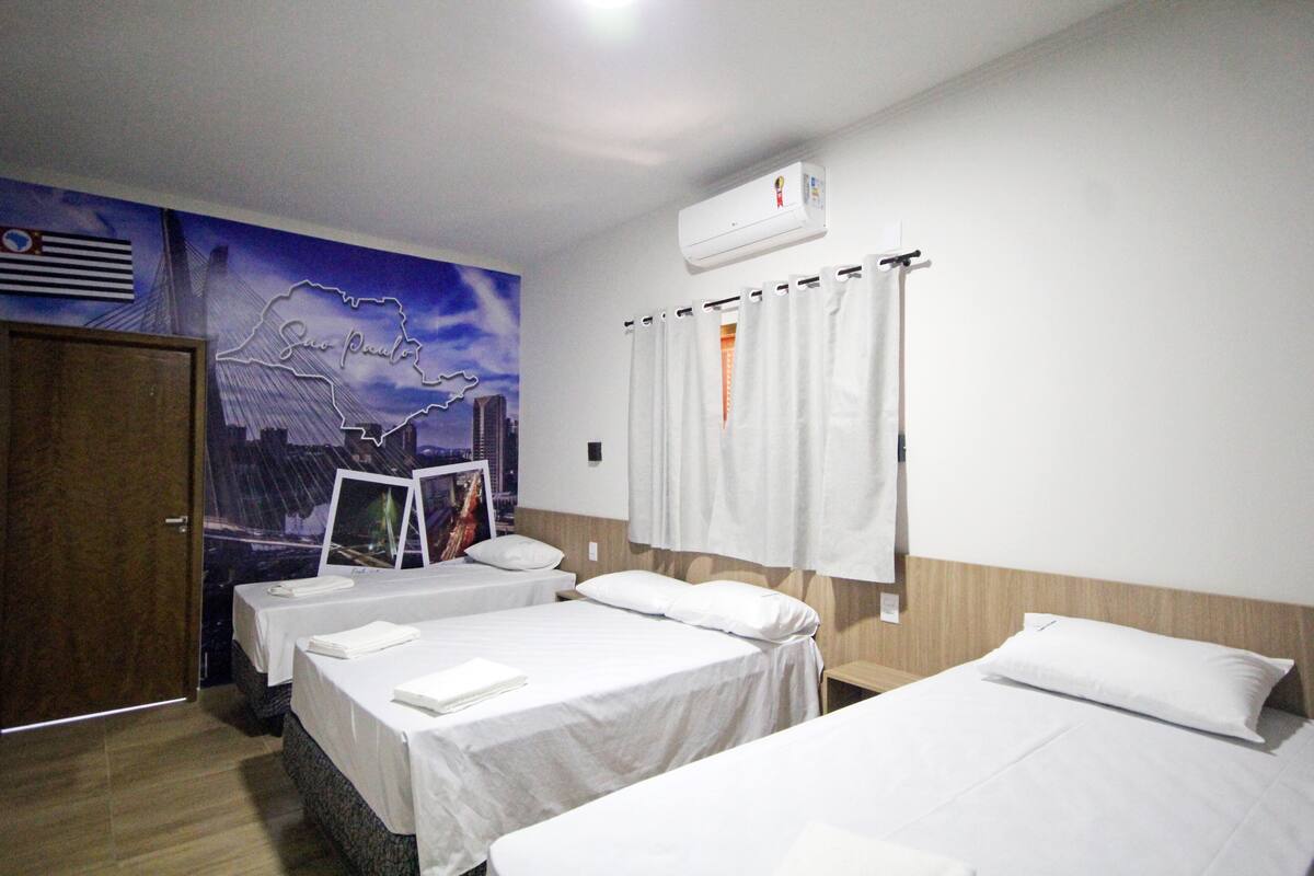 Ein Hotelzimmer mit zwei Betten, einem Stadtbild-Wandgemälde, einer Klimaanlage und einer Vorhangstange.