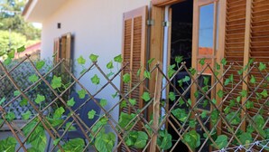 A building with wooden shutters, a metal fence, and green foliage. - Pousada das Bandeiras (Olímpia)