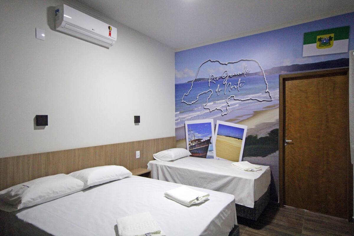 Ein Hotelzimmer mit zwei Betten, einem Wandgemälde von Rio Grande do Norte und einer Holztür.