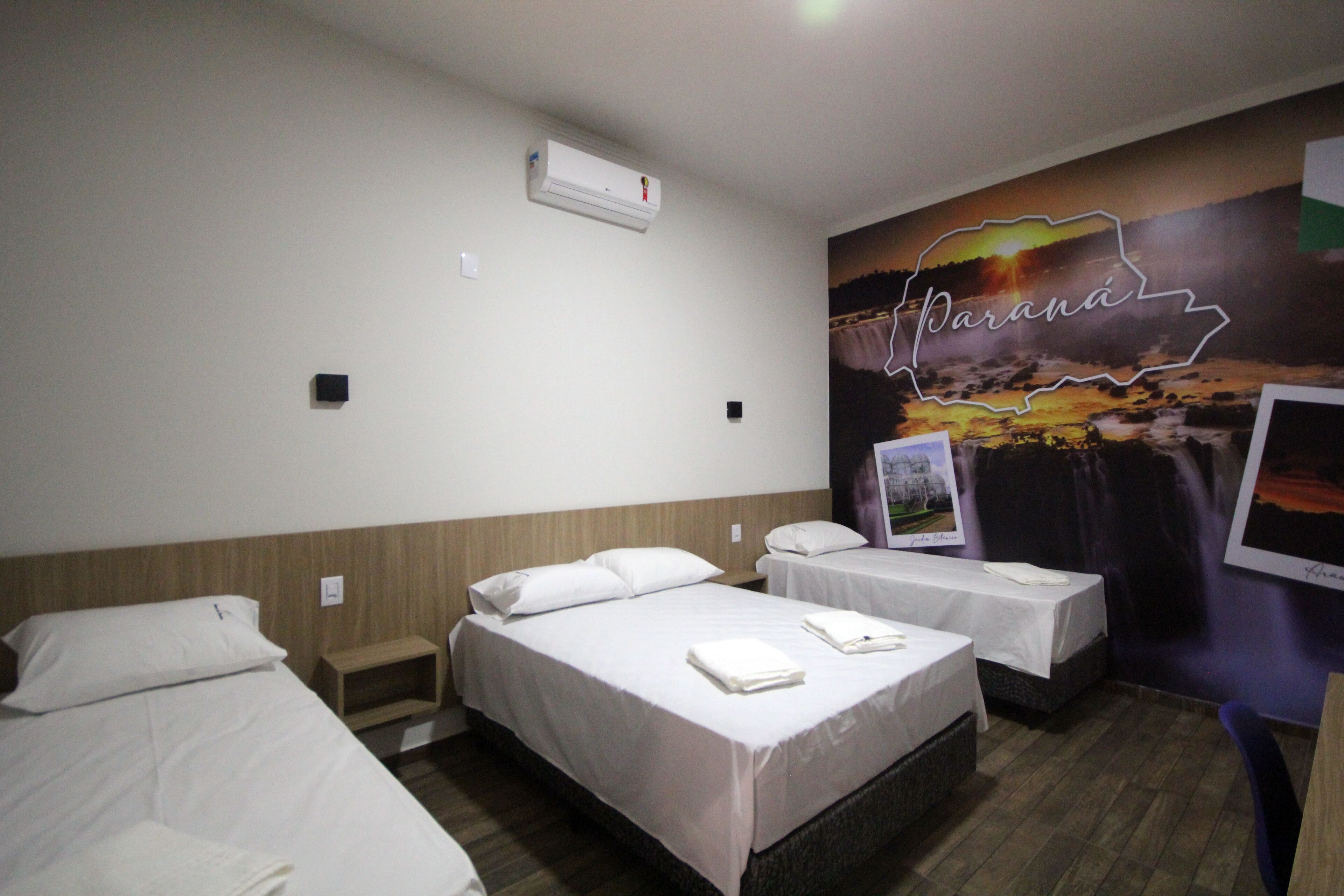 Une chambre d’hôtel avec deux lits, un climatiseur fixé au mur et une fresque représentant un paysage avec le mot « Parana ».