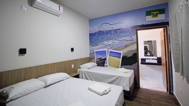 A hotel room with two beds, an air conditioner, a wall mural, and a bathroom visible through an open door. - Pousada das Bandeiras (Olímpia)