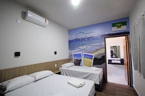 A hotel room with two beds, an air conditioner, a wall mural, and a bathroom visible through an open door.
