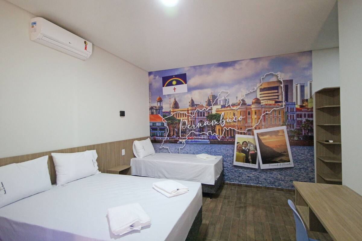 Ein Hotelzimmer mit zwei Betten, einem Wandbild einer Stadtansicht und einer Wand-Klimaanlage.