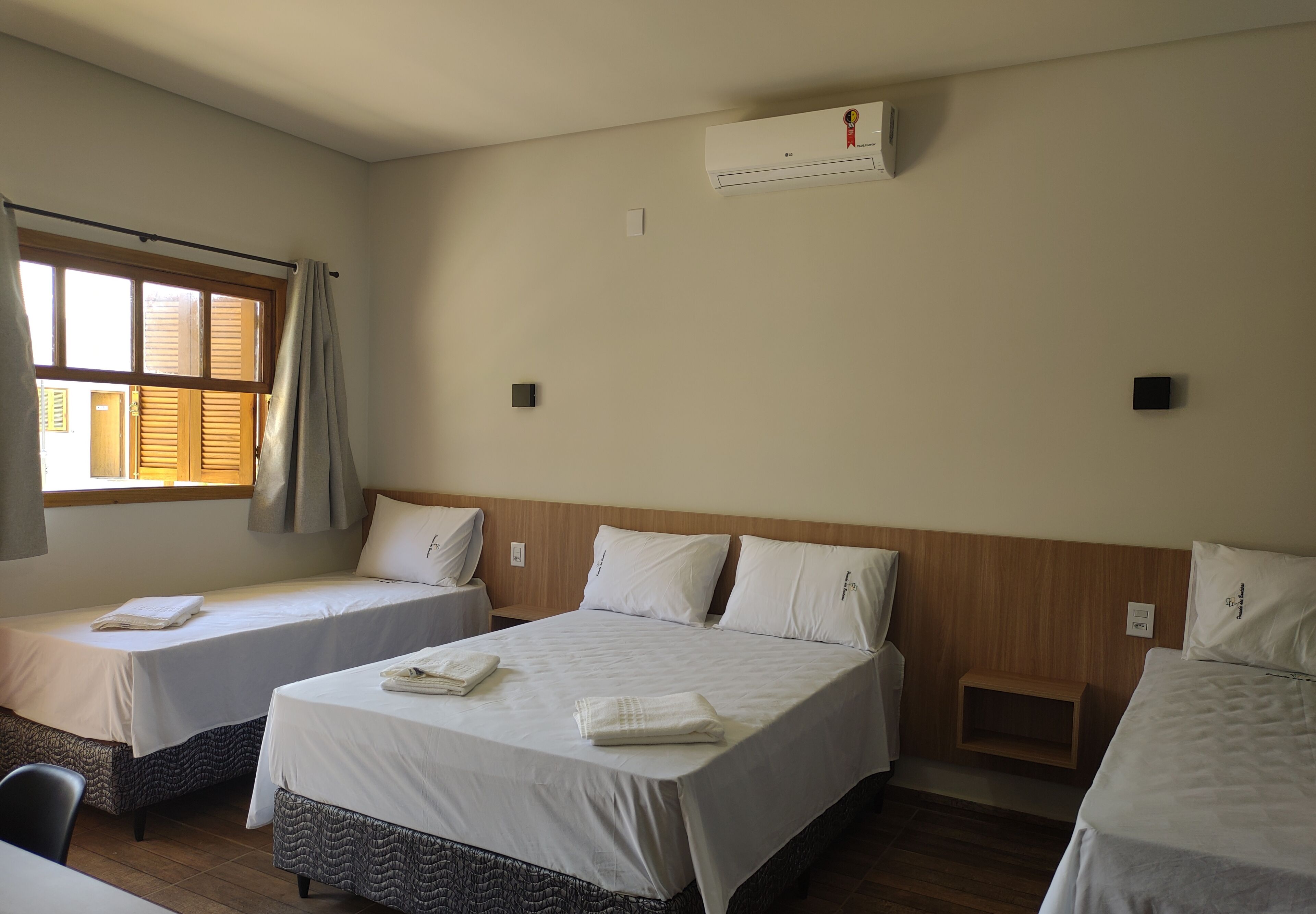 Una habitación de hotel con dos camas individuales, cabecera de madera, aire acondicionado y una ventana con cortinas.