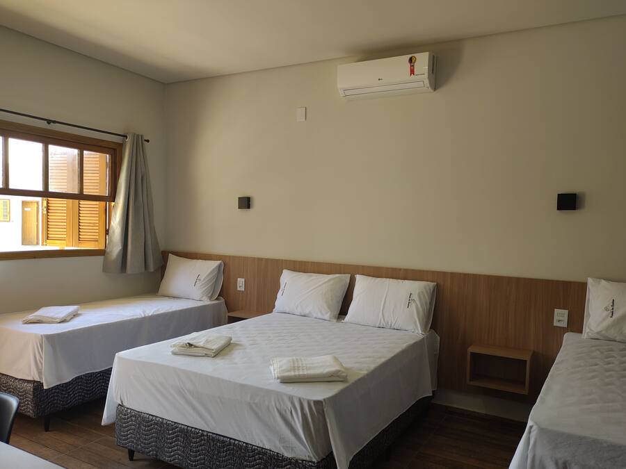 Una habitación de hotel con dos camas individuales, cabecera de madera, aire acondicionado y una ventana con cortinas.