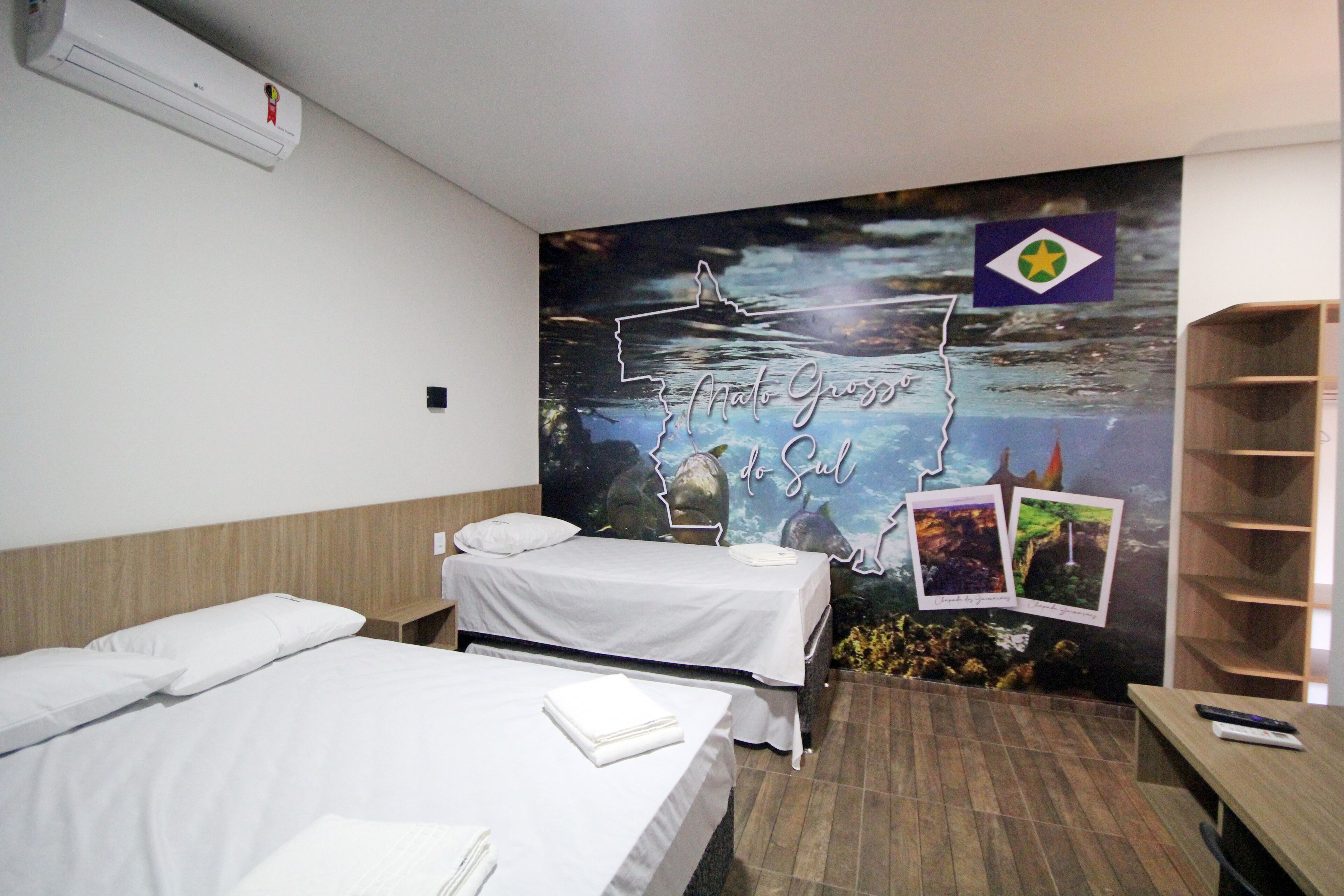 Habitación de hotel con dos camas, un mural en la pared, un estante de madera y una mesita.