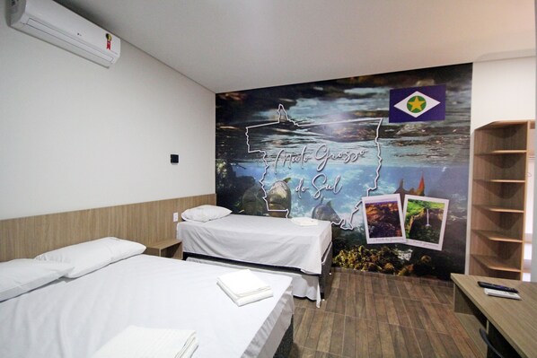 Habitación de hotel con dos camas, un mural en la pared, un estante de madera y una mesita.