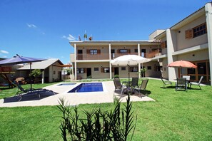 A hotel with a swimming pool, outdoor seating, and a well-maintained lawn.