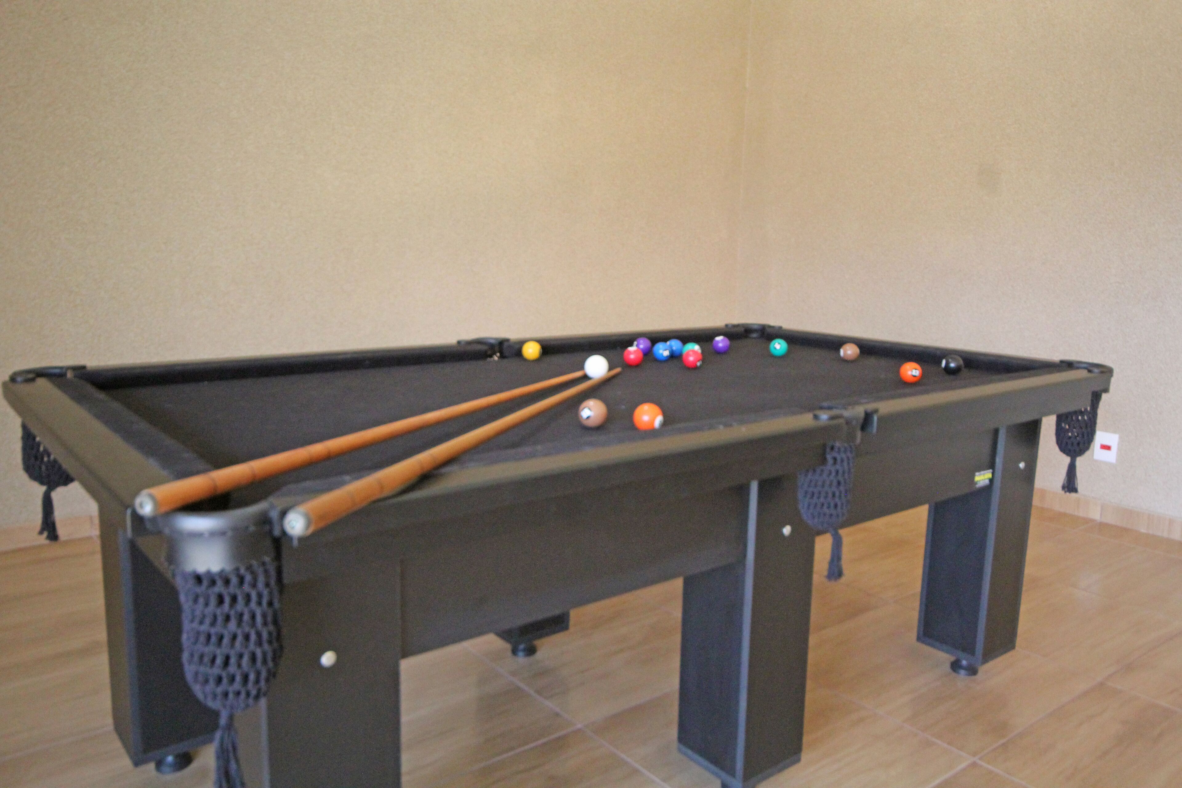 A pool table with a variety of colored balls and cues, set against a plain wall.
