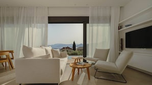 Una sala de estar moderna con sofá, sillón y mesa de centro, un televisor de pantalla plana y vistas a las montañas a través de grandes ventanales.