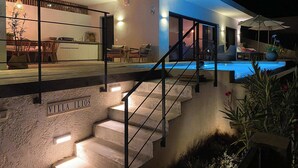 Una villa moderna con piscina, zona de comedor y escalera que lleva a la planta superior.