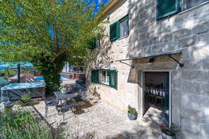 A stone building with a patio, outdoor seating, a hot tub, and a view of a pool and mountains.