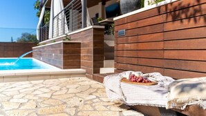 Un área junto a la piscina con suelo de baldosas de piedra, un banco de madera con tela y una pared de madera.