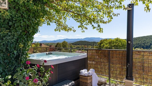 Un jacuzzi rodeado de follaje, un banco de madera y una cesta de mimbre con toallas.