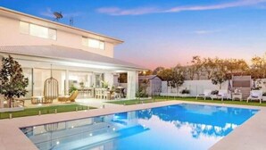 A modern house with a swimming pool, a covered patio, and a well-maintained lawn.