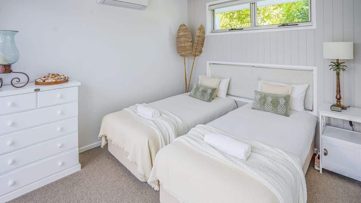 A bedroom with two beds, a dresser, a nightstand, and a window with a view of greenery.