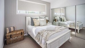 A bedroom with a large bed, a mirror, a chest of drawers, and a window with blinds.