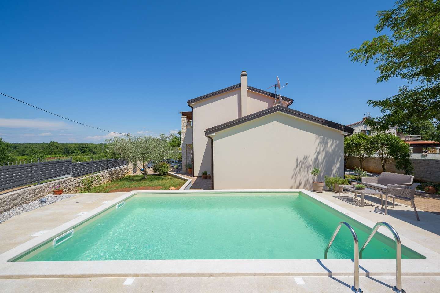 A swimming pool with a clear blue water, a small building with a sloped roof, and a stone wall in the background.
