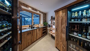 A modern kitchen with wooden cabinetry, a wine refrigerator, and a view of the outdoors. - Naturhotel Waldheim (Anterivo)