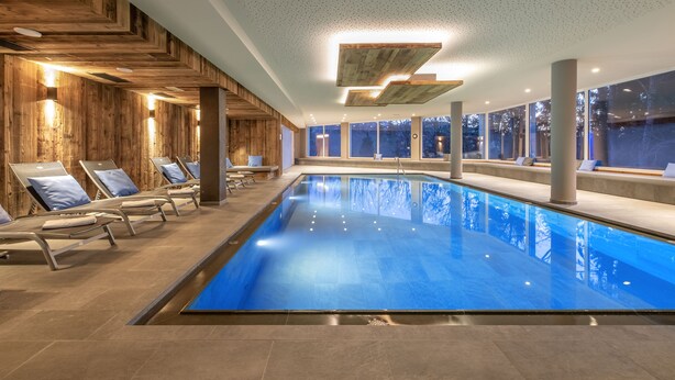 A modern indoor swimming pool with wooden paneling and lounge chairs. - Naturhotel Waldheim (Anterivo)