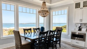 Zona pranzo con vista sulla spiaggia, un lampadario e una cucina con armadi.