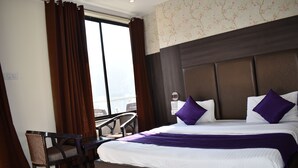 A hotel room with a large bed, two pillows, a desk, and a chair. - Tapasthali By Meera Hotels (Narendranagar)