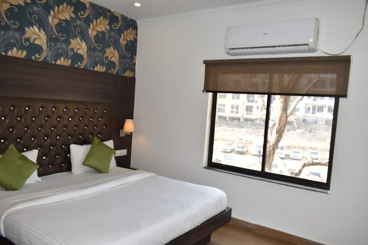 Quarto de hotel com cama, cabeceira, janela com vista para carros estacionados e edifícios, e um aparelho de ar condicionado.
