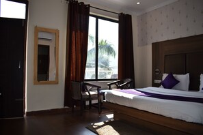 A hotel room with a bed, a desk, and a window with curtains.