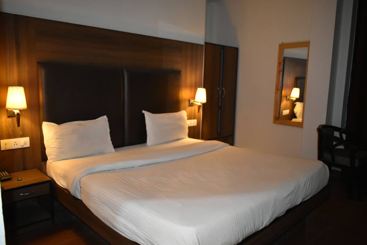 Quarto de hotel com uma cama grande, duas luminárias de cabeceira, uma mesa de cabeceira e um espelho na parede.