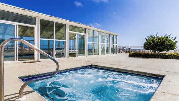 Una piscina con una escalera de metal, un edificio de cristal con ventanas grandes y un cielo azul despejado.